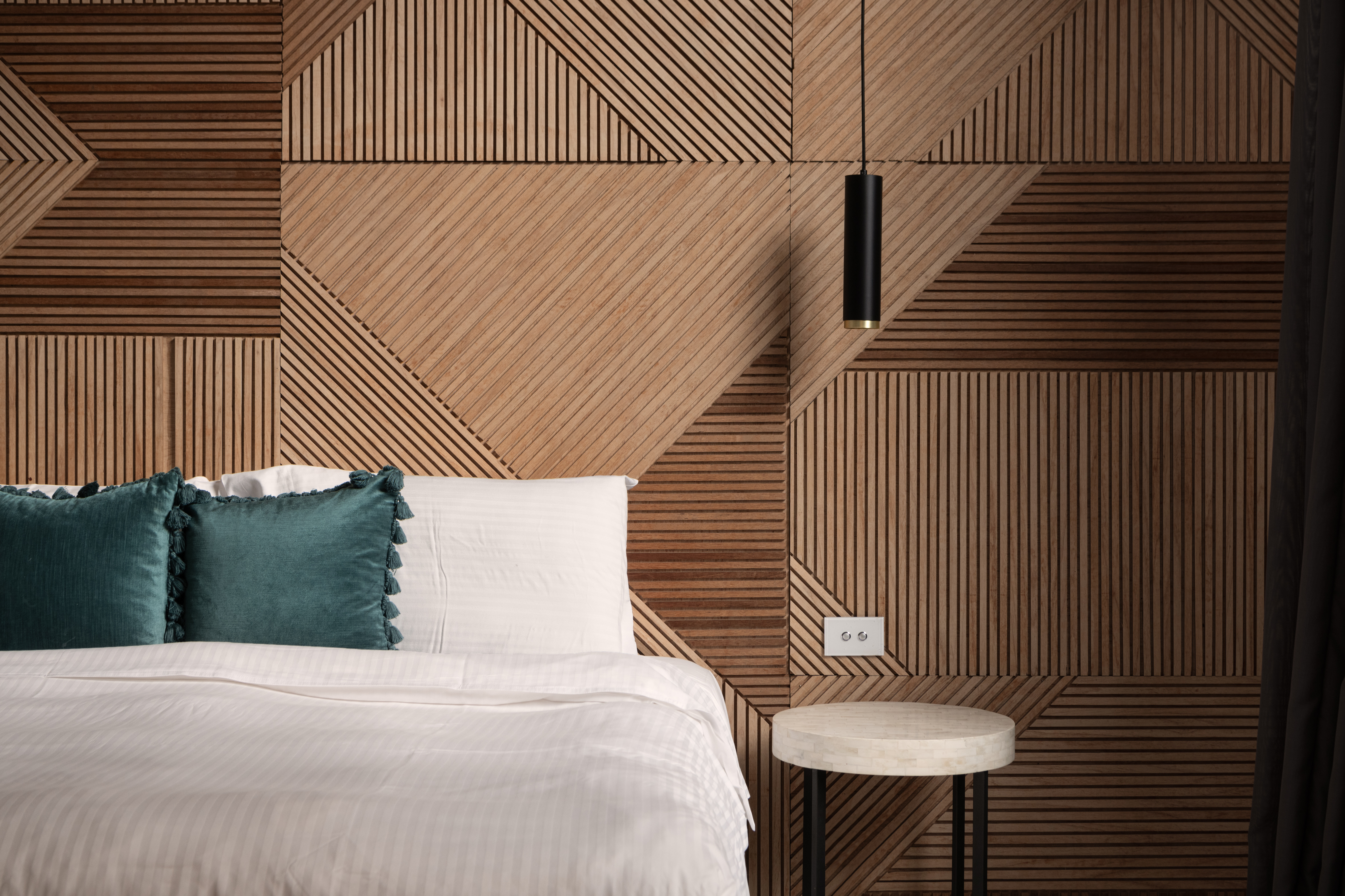 bed-with-pillows-and-geometric-timber-and-wood-pattern-wall-and-hanging-light-close-up-beautiful-abstract-well-interior-design-luxurious-bedroom-filled-with-natural-light-wood-accent-wall